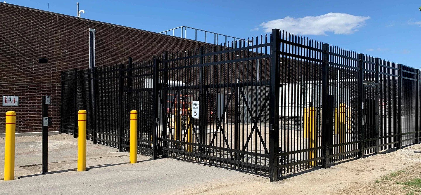 Black metal security fence with spiked tops and yellow bollards